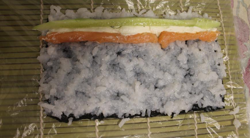Выложить тонким слоем рис на лист нори, затем начинку