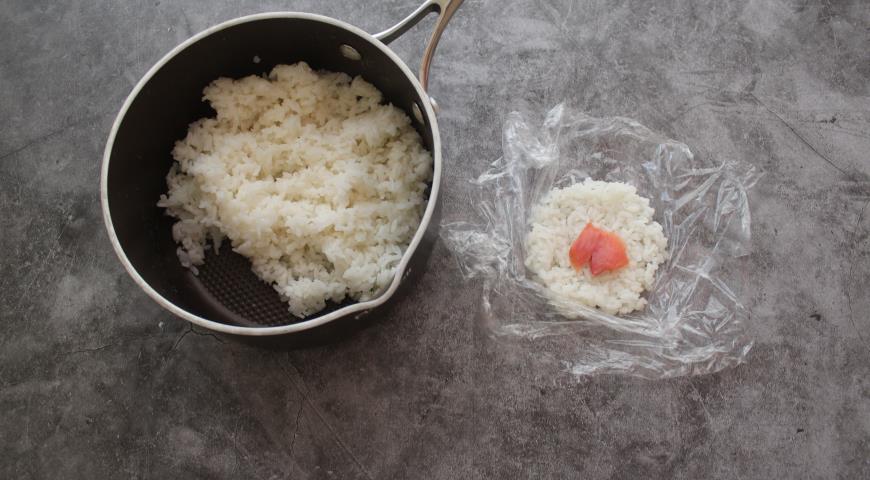 Выкладываем отварной рис для суши на пищевую пленку в виде круга, в центр кладем кусочки рыбы
